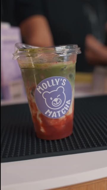 Ein Iced Strawberry Matcha im Becher mit Bär-Sticker auf der schwarzen Barmatte