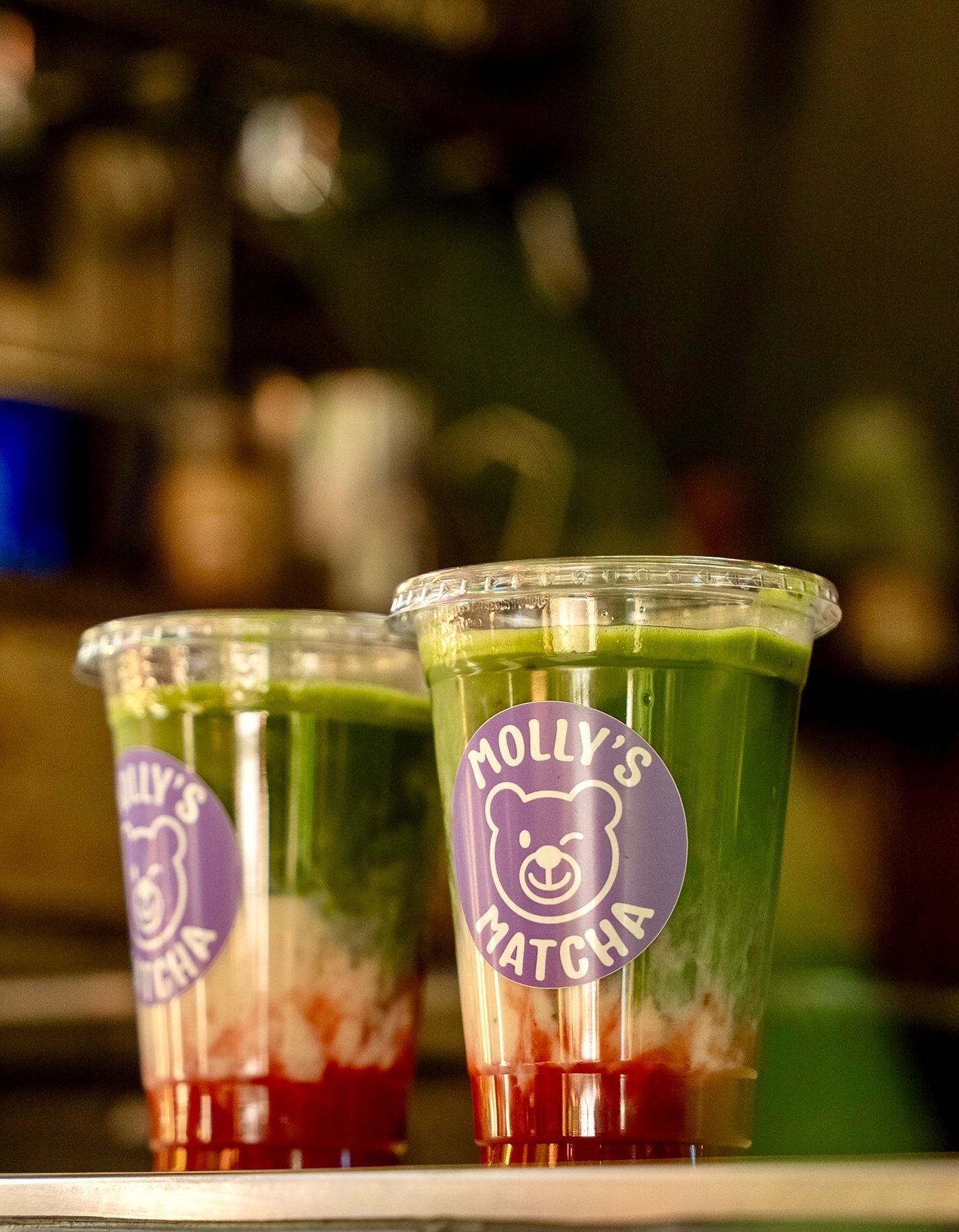 Zwei Iced Strawberry Matcha im Becher mit Bär-Sticker auf dem Tresen