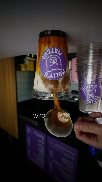 Ein Specialty Iced Latte wird eingeschenkt, daneben Becher mit Bär-Sticker