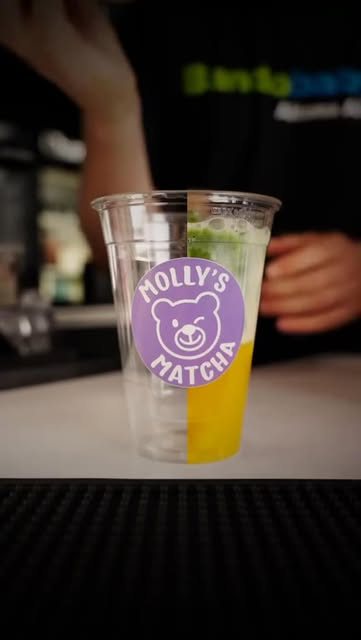 Ein Becher mit Matcha-Limonade, halb grün, halb gelb, mit Bär-Sticker